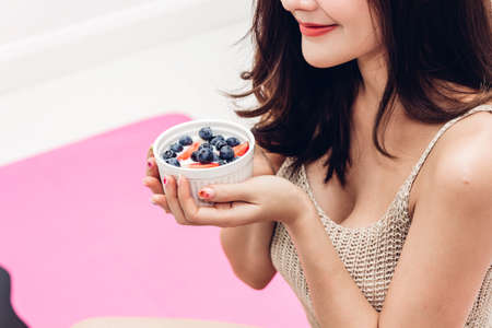 Fitness woman holding yogurt and mixed berries blueberries with strawberries while relaxing at home.dieting concept.healthy lifestyleの写真素材