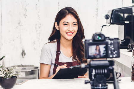 Portrait of woman barista blogger in front of camera recording herself behind the counter bar in a cafeの写真素材