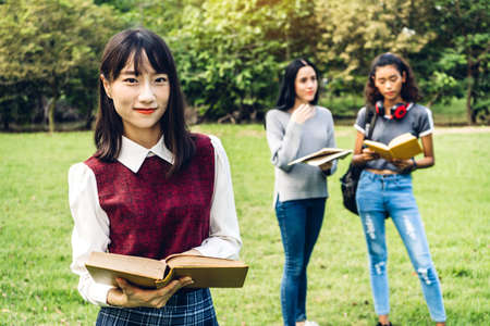 Smiling woman international students or teenagers standing and holding book smiling at camera with group of students in park at university.Education and friendship Conceptの写真素材