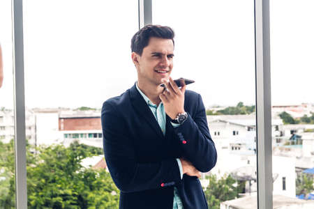 Portrait of handsome businessman in black suit standing and using smartphone outdoors in modern office.man working with technology devices conceptの写真素材