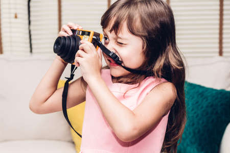 Little cute girl taking a picture with vintage camera at homeの写真素材