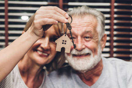Senior couple holding key together sitting on sofa in living room from new house.Retirement couple and real estate conceptの写真素材