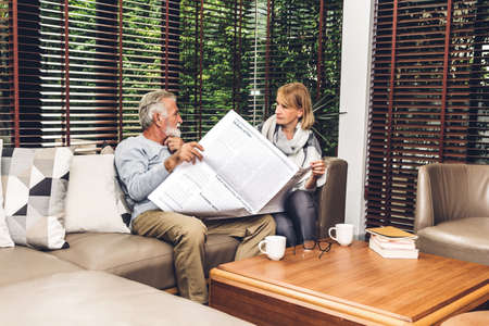 Senior couple relax talking and reading newspaper together on sofa in living room at home.Retirement couple conceptの写真素材