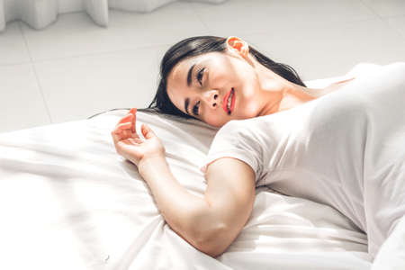 Beautiful woman relaxing on the bed in her room at homeの写真素材