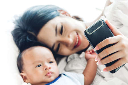 Mother with baby use smartphone in a white bedroom.Love of family conceptの写真素材