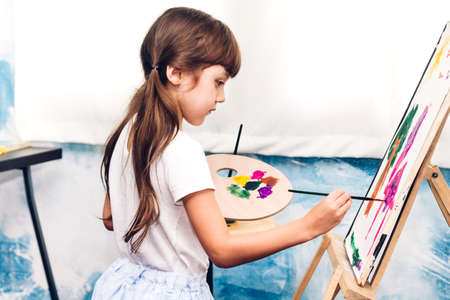Little girl artist drawing on canvas with color palette and watercolor paints at homeの写真素材