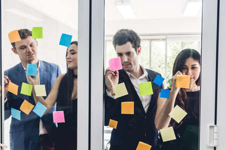 Group of casual business people planning and brainstorm writing over the project with stickers note on glass window at modern office.Teamwork conceptの写真素材