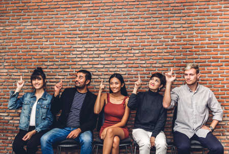 Group of business people while sitting on chair pointing to empty copy space against wall background