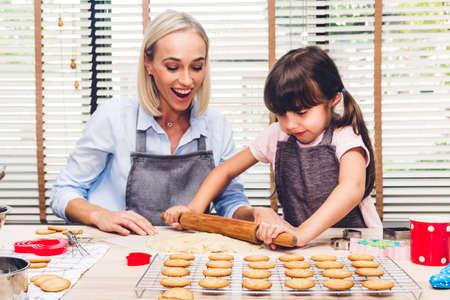 Mother and daugthter having fun cooking togather and learning to make a cake while baking in kitchen at homeの写真素材