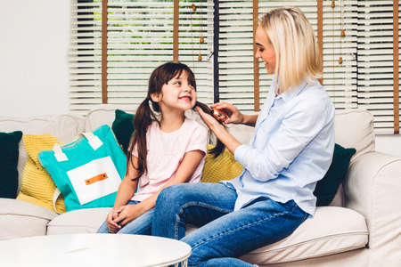 Mother with little daughter packing school bag with books before going to school at home