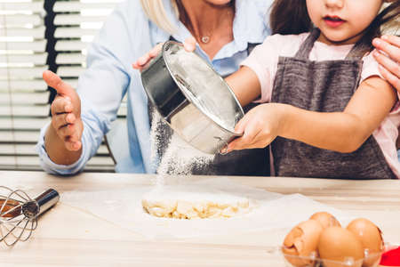 Mother and daugthter having fun cooking togather and learning to make a cake while baking in kitchen at homeの写真素材