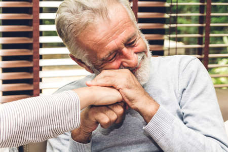 Happy smiling elder senior couple hugging relaxing and talking together sitting on sofa in living...