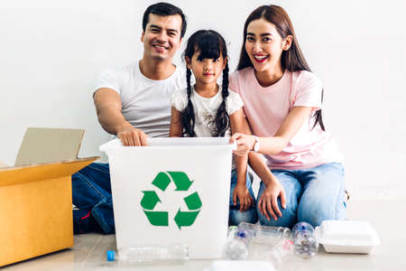Happy smiling family having fun putting empty recycling plastic bottles and paper into the recycle boxの写真素材