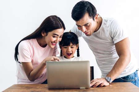 Happy family father and mother with daughter sitting and looking at laptop computer together in the living room at homeの写真素材