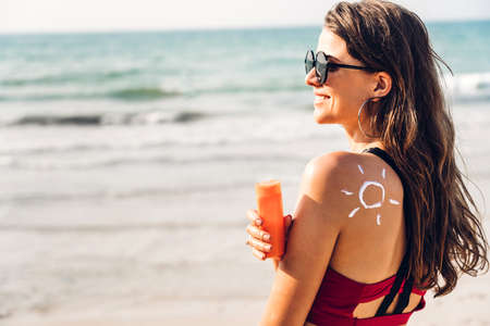 Woman wearing two piece bikini applying suncream with sun drawn on back on the tropical beach.Summer...