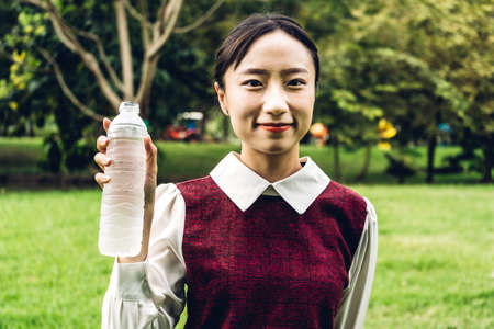 Beautiful asia woman drinking water from a bottle while relaxing and feeling fresh on green natural background at summer green park. Healthy lifestyle conceptの写真素材