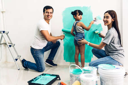 Happy family using a paint roller and painting walls in their new homeの写真素材