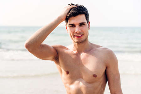 Portrait of smiling handsome sexy man showing muscular fit body standing on the tropical beach.Summer vacationsの写真素材