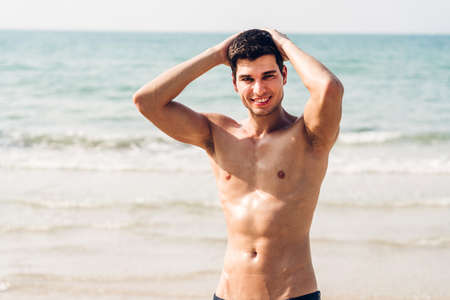 Portrait of smiling handsome sexy man showing muscular fit body standing on the tropical beach.Summer vacationsの写真素材