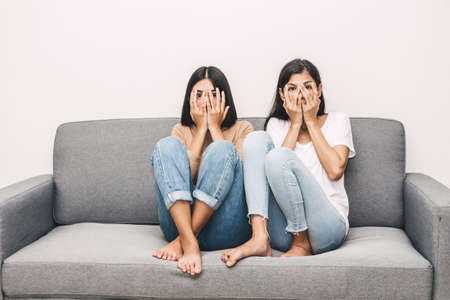 Two scared women on couch watching  horror movie on TV at homeの写真素材