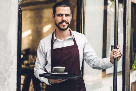 Portrait of handsome bearded barista man small business owner smiling and holding cup of coffee...