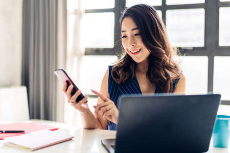 Businesswoman sitting and working with laptop computer and use smartphone.creative business people planning in her workstation at modern work loftの写真素材