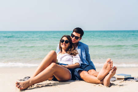 Young couple with coconut juice and book on the tropical beach.Couple relaxing on the beach.Summer vacationsの写真素材