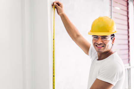 Young construction engineer in a yellow helmet working and  making measurements on the wall at building home siteの写真素材