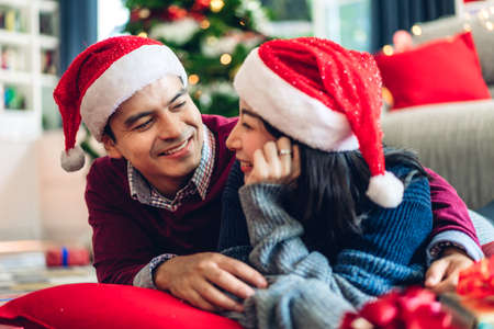Romantic sweet couple in santa hats having fun and smiling while celebrating new year eve and enjoying spending time together in christmas time at homeの写真素材