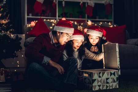 Portrait of happy family father and mother with daughter in santa hats having fun opening magic christmas gift box and enjoying spending time together in christmas time at homeの写真素材