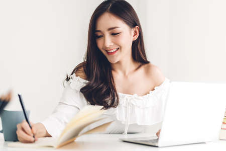 Girl student sitting and studying and learning online with laptop computer and writing a book before...