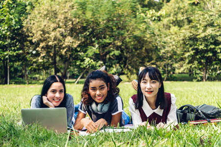 Group of smiling international students or teenagers using laptop computer doing their homework with book together in park at university.Education and friendship Conceptの写真素材
