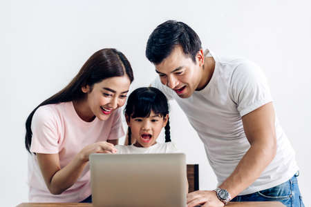 Happy family father and mother with daughter sitting and looking at laptop computer together in the living room at home