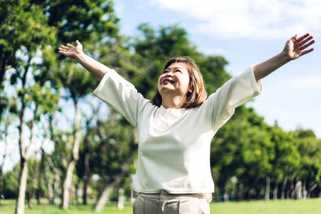 Portrait of happy senior adult elderly asia women smiling standing and stretch her arms relax and enjoy with nature fresh air in the parkの写真素材