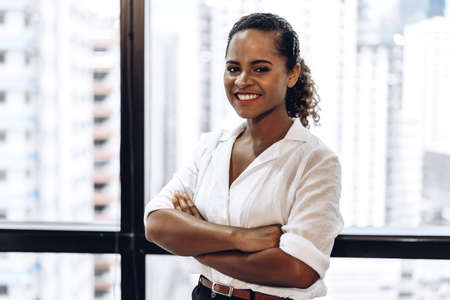 Smiling beautiful professional business african american black woman with arms crossed standing in officeの写真素材