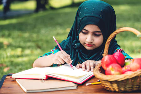 Portrait of happy little muslim girls child with hijab dress smiling and enjoy relax reading and write a book in summer park.Education conceptの写真素材