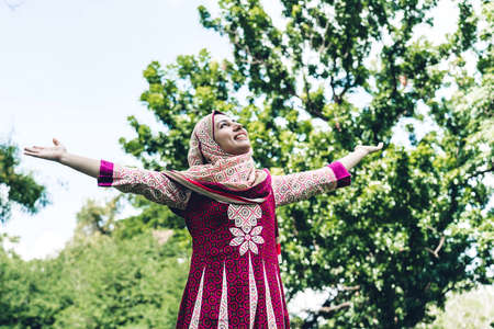 Portrait of happy arabic muslim woman with hijab dress  smiling standing and stretch her arms relax and enjoy with nature fresh air in the parkの写真素材