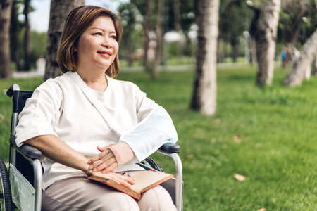 Senior adult elderly asia women sit on wheelchair and reading book outdoorの写真素材