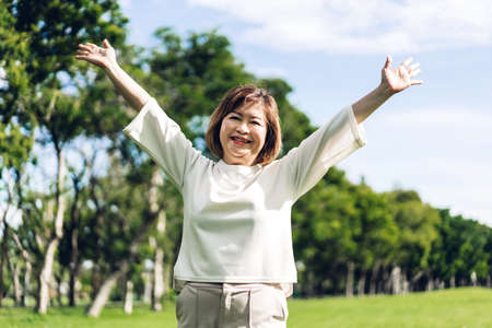 Portrait of happy senior adult elderly asia women smiling standing and stretch her arms relax and enjoy with nature fresh air in the parkの写真素材