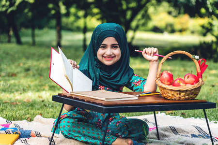 Portrait of happy little muslim girls child with hijab dress smiling and enjoy relax reading and write a book in summer park.Education conceptの写真素材