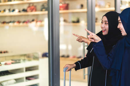 Two young asian muslim woman enjoying shopping and having fun pointing finger in the shop window outdoors at fashion storeの写真素材