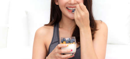 Fitness woman holding yogurt and mixed berries blueberries with strawberries while relaxing at...