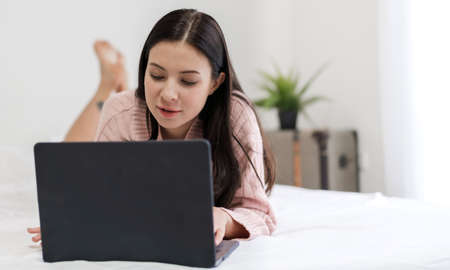 Smiling of young beautiful pretty woman relaxing and using technology laptop computer lying on bed and joyful on weekend in the bedroom.girl checking social apps and working.technology online conceptの写真素材