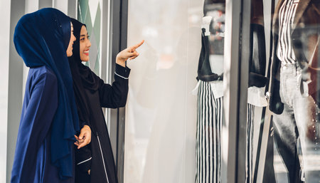 Two young asian muslim woman enjoying shopping and having fun pointing finger in the shop window outdoors at fashion storeの写真素材