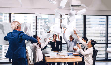 Successful group of casual business relaxing and throwing paper in modern work loft.Creative business people celebrating with arms up.Teamwork and success conceptの写真素材