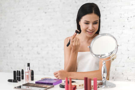 Smiling of young beautiful pretty woman clean fresh healthy white skin looking at mirror.girl holding make-up brushes and make up on face with cosmetics set at home.facial beauty and cosmetic conceptの写真素材