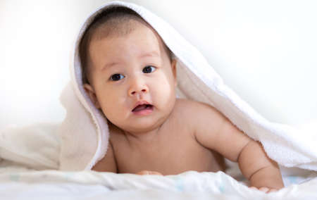 Portrait of happy asian smile baby relaxing under towel after bath on the bedの写真素材