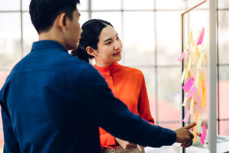 Two casual business people planning and brainstorm writing over the project with stickers note on glass window at modern office.Teamwork conceptの写真素材