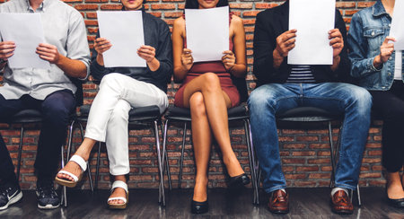 Group of business people holding paper while sitting on chair waiting for job interview against wall backgroundの写真素材