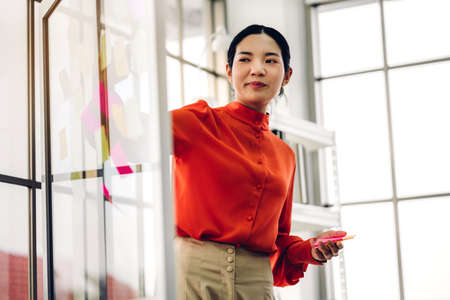 Casual business woman planning and brainstorm writing over the project with stickers note on glass window at modern officeの写真素材